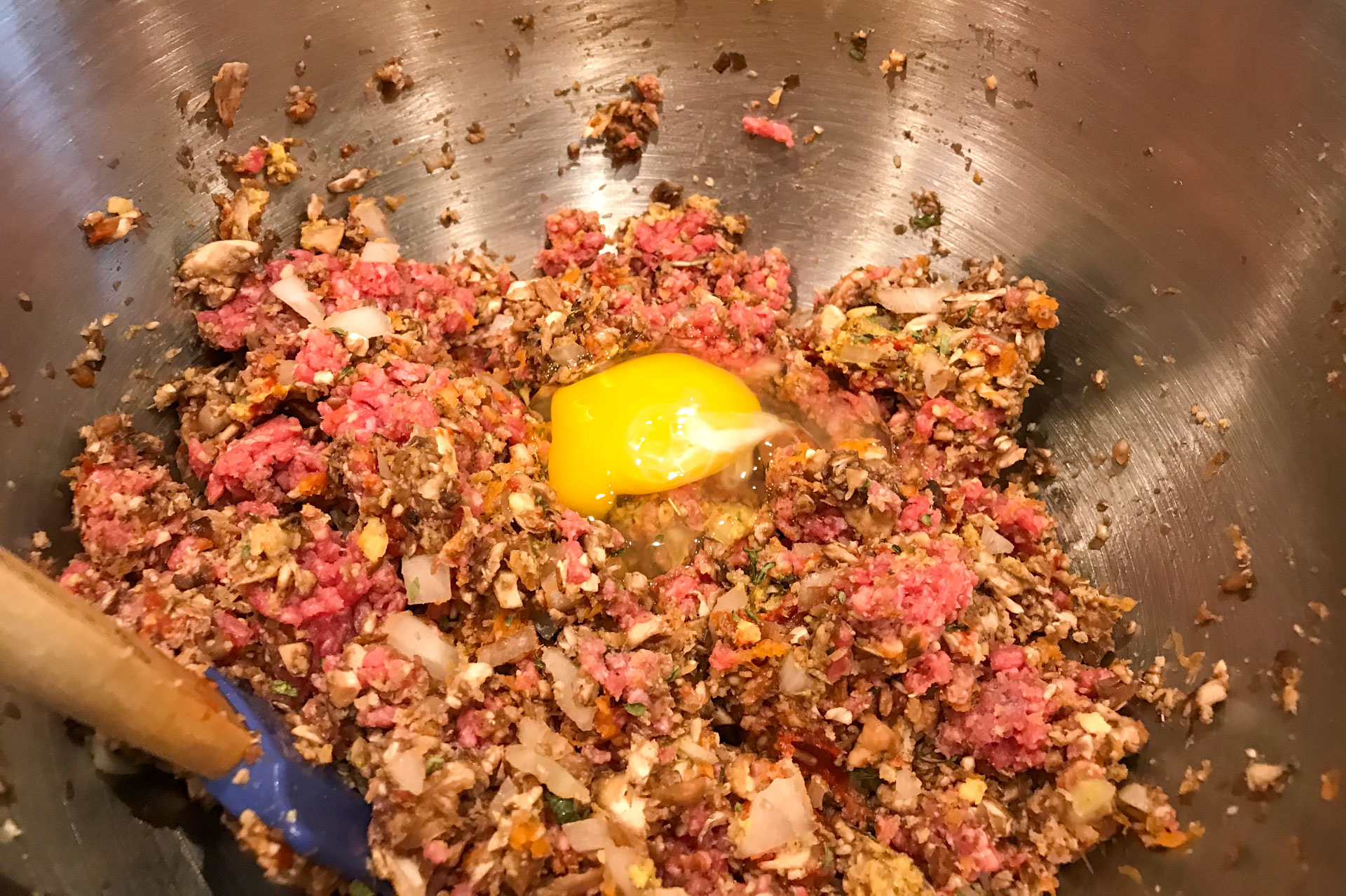 meatloaf mixture: raw egg on top of ground meat and vegetable mixture in a stainless steel mixing bowl