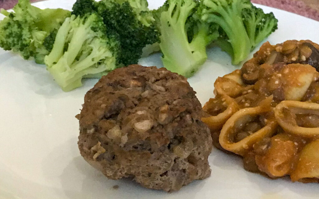 muffin tin meatloaf plated with broccoli and a lentil and pasta mixture on a white plate