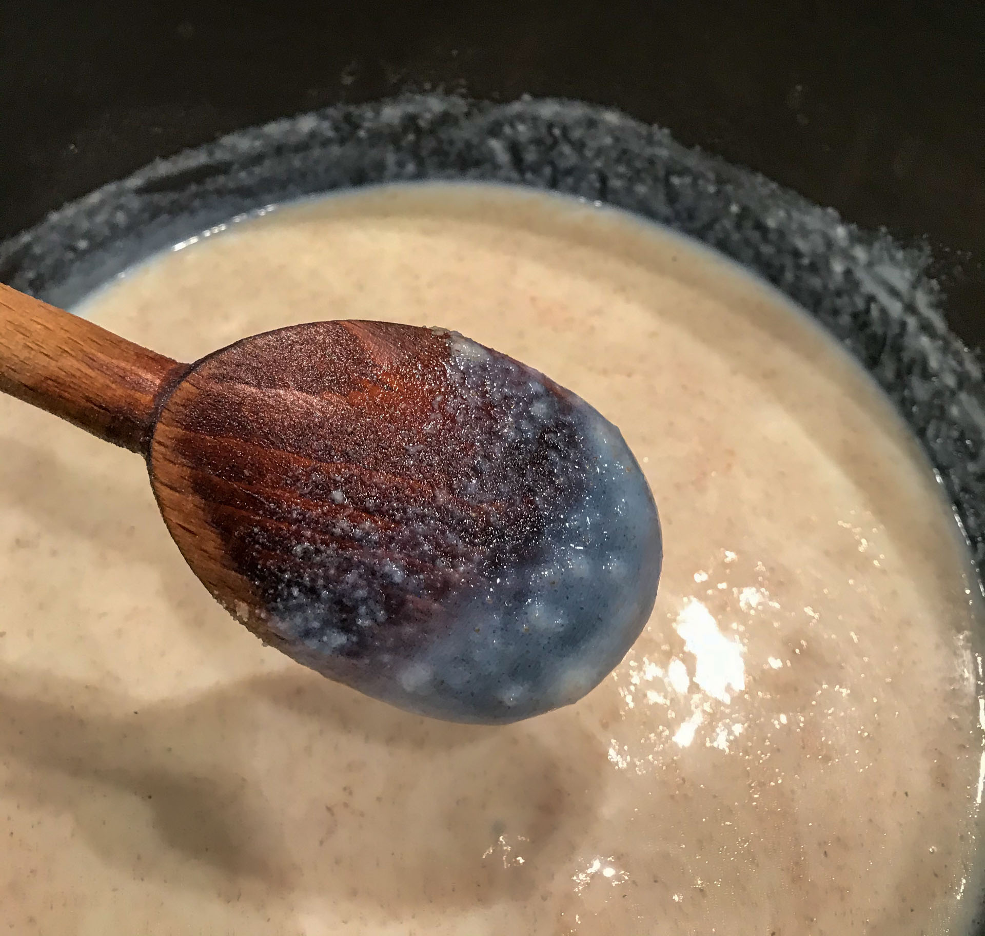 white sauce in cast iron pan, with some sauce coating the back of a wooden spoon